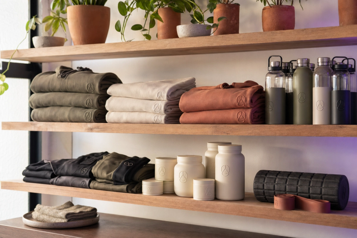 Clean retail shelf inside a boutique fitness studio displaying neatly folded branded apparel, water bottles, and supplements.