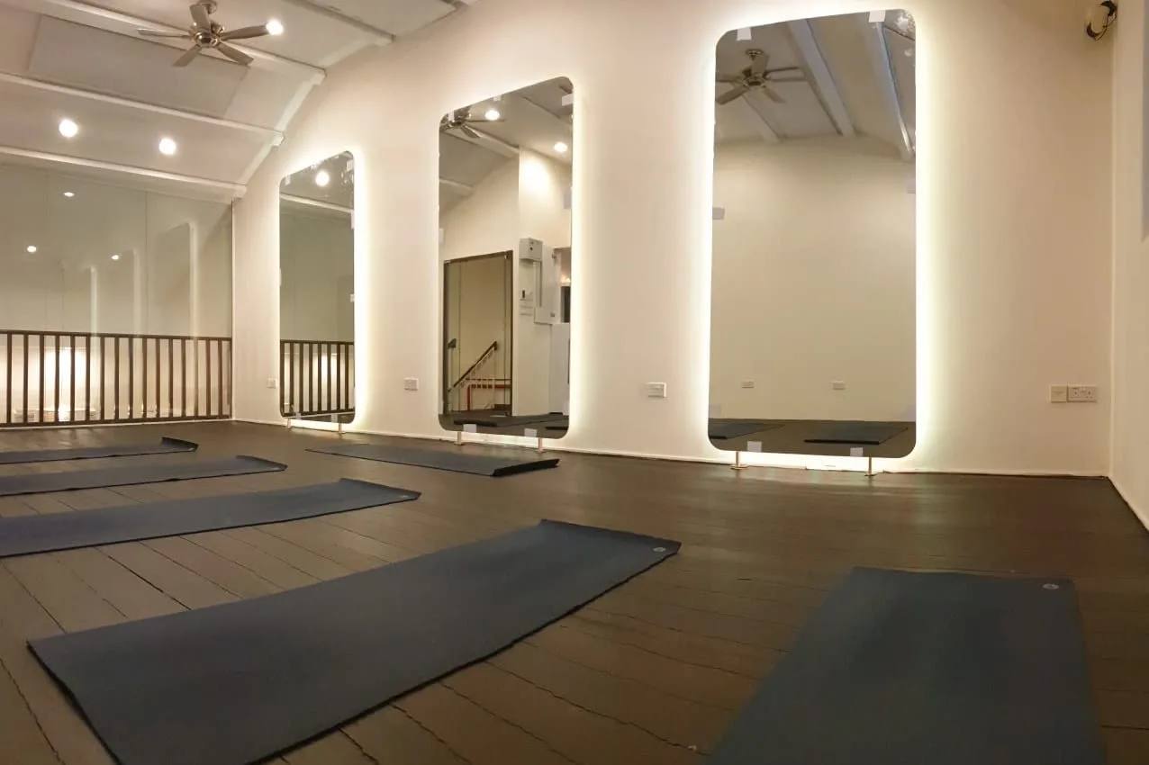 Shiva Yoga Studio practice room in Singapore, dark timber floor with mats laid out and backlit full-length mirrors along the wall