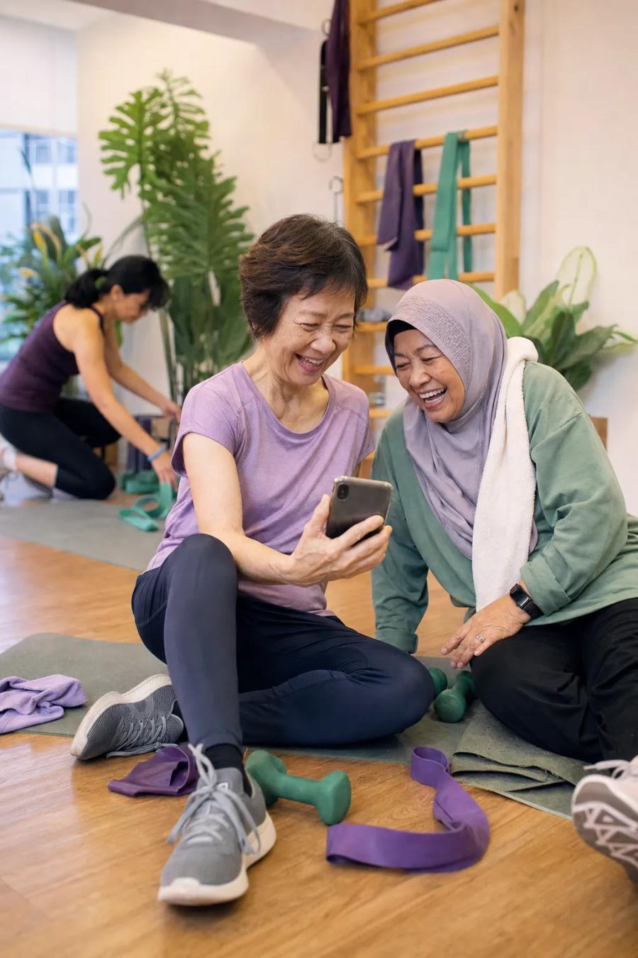 Two senior members laugh together over a phone after their small-group strength class.