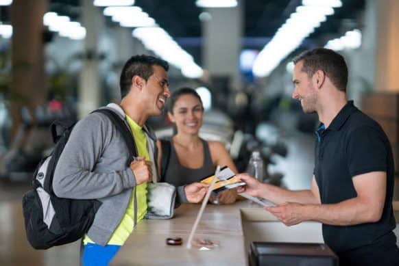 Happy couple of people at the gym talking to the receptionist about membership plans - healthy lifestyle concepts