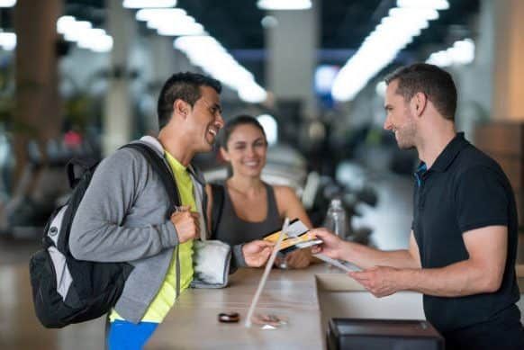 Happy couple of people at the gym talking to the receptionist about membership plans - healthy lifestyle concepts