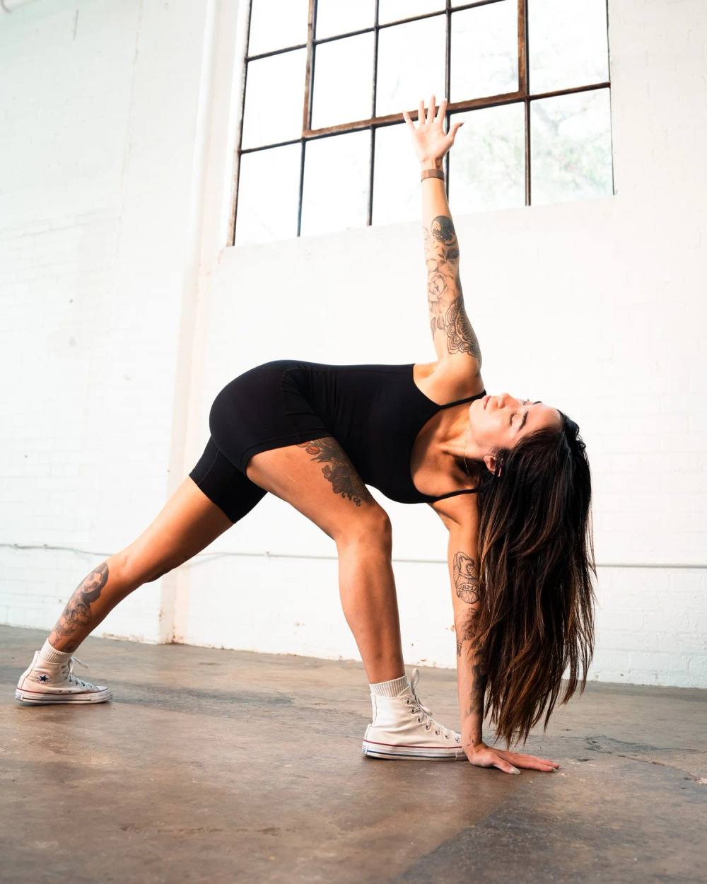 SYMONE Yoga in Texas, a yoga practitioner moving through a standing pose in a bright white-brick studio with tall industrial windows