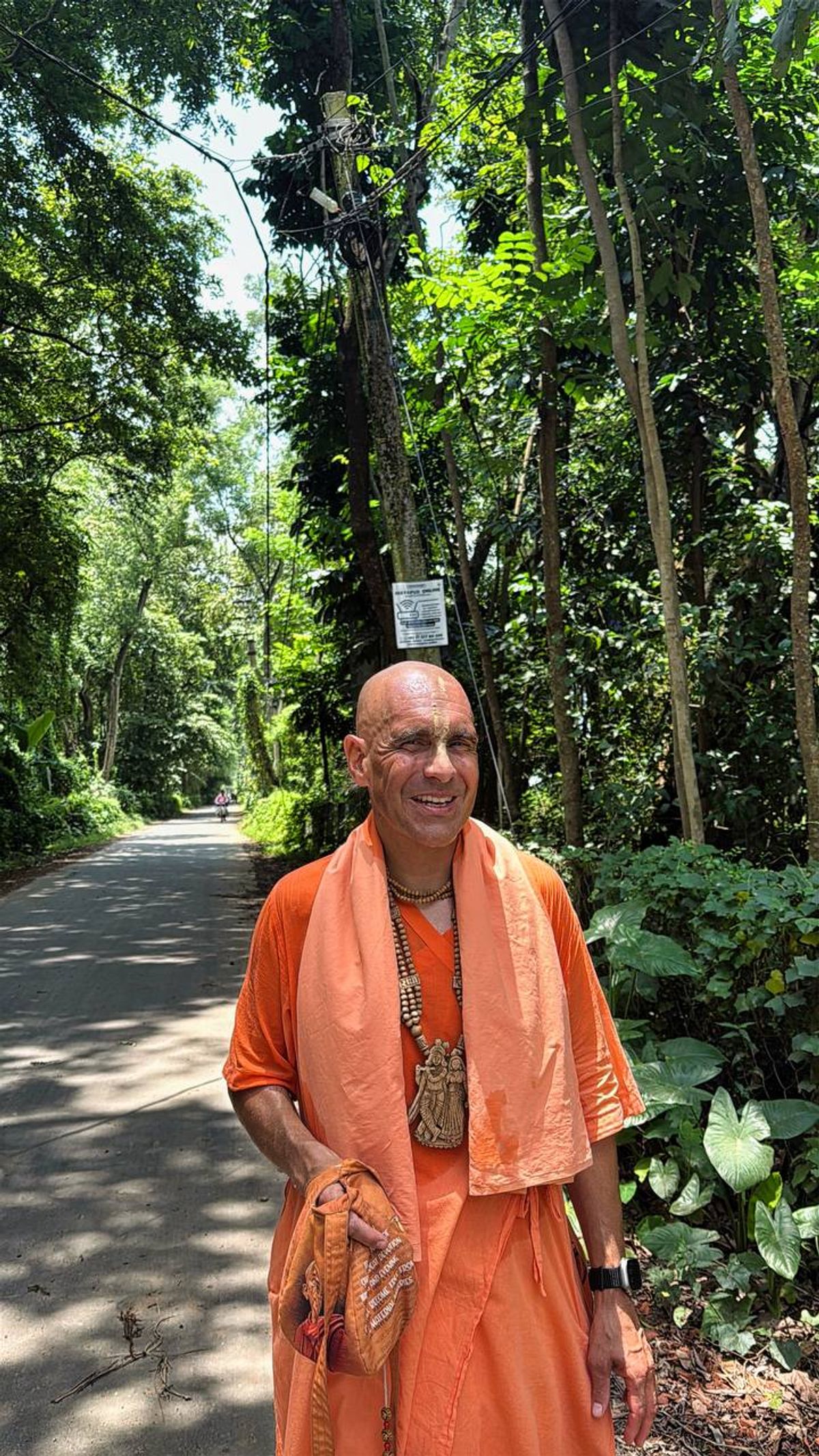 A devotee in orange robes on a tree-lined path