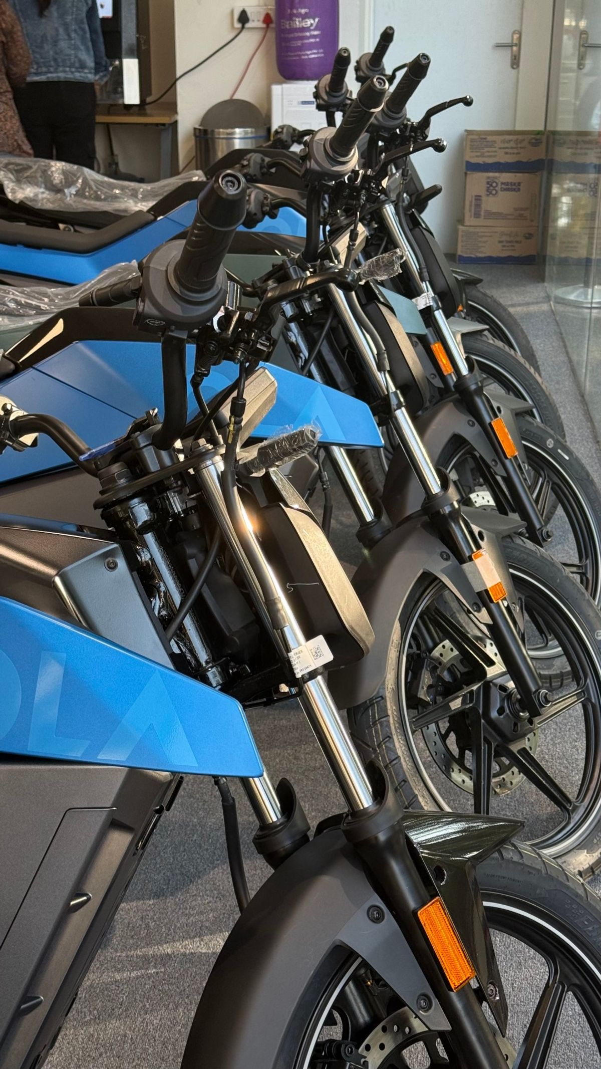 Row of blue Ola Roadster electric motorcycles on display