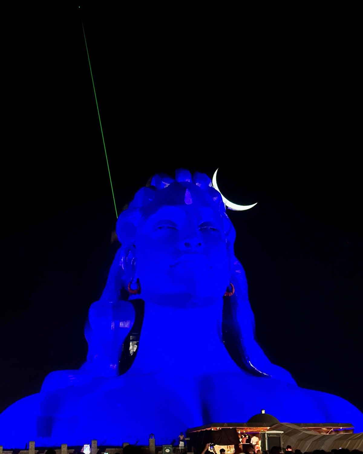 Adiyogi statue illuminated in blue with laser beams at night