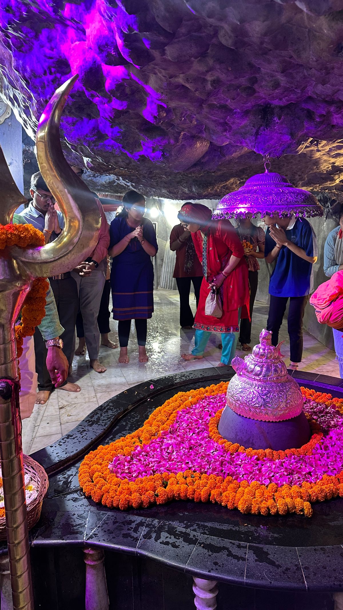 Shivalingam decorated with marigold and pink flowers in a cave shrine
