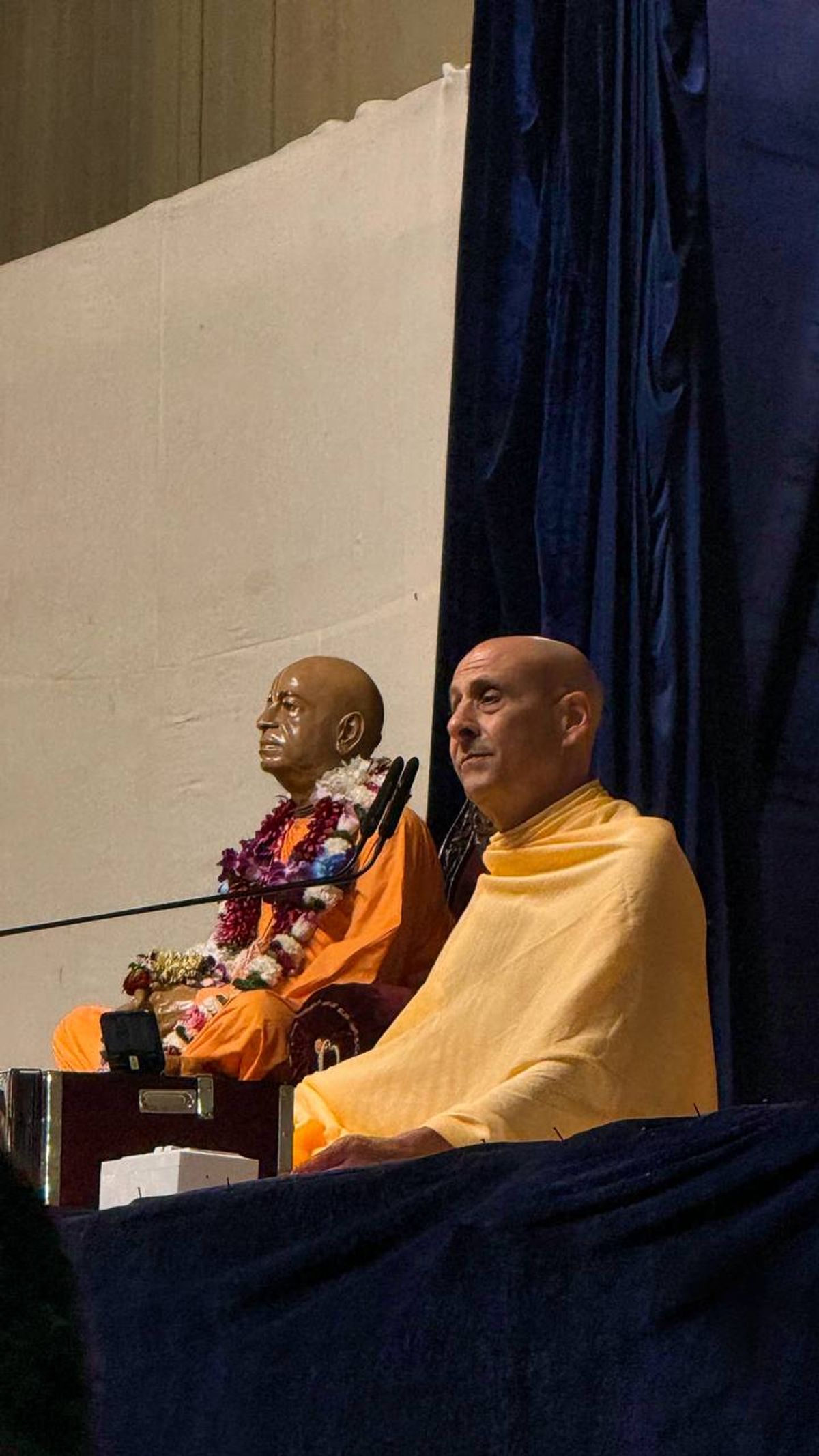 Radhanath Swami giving a lecture next to a murti of Srila Prabhupada