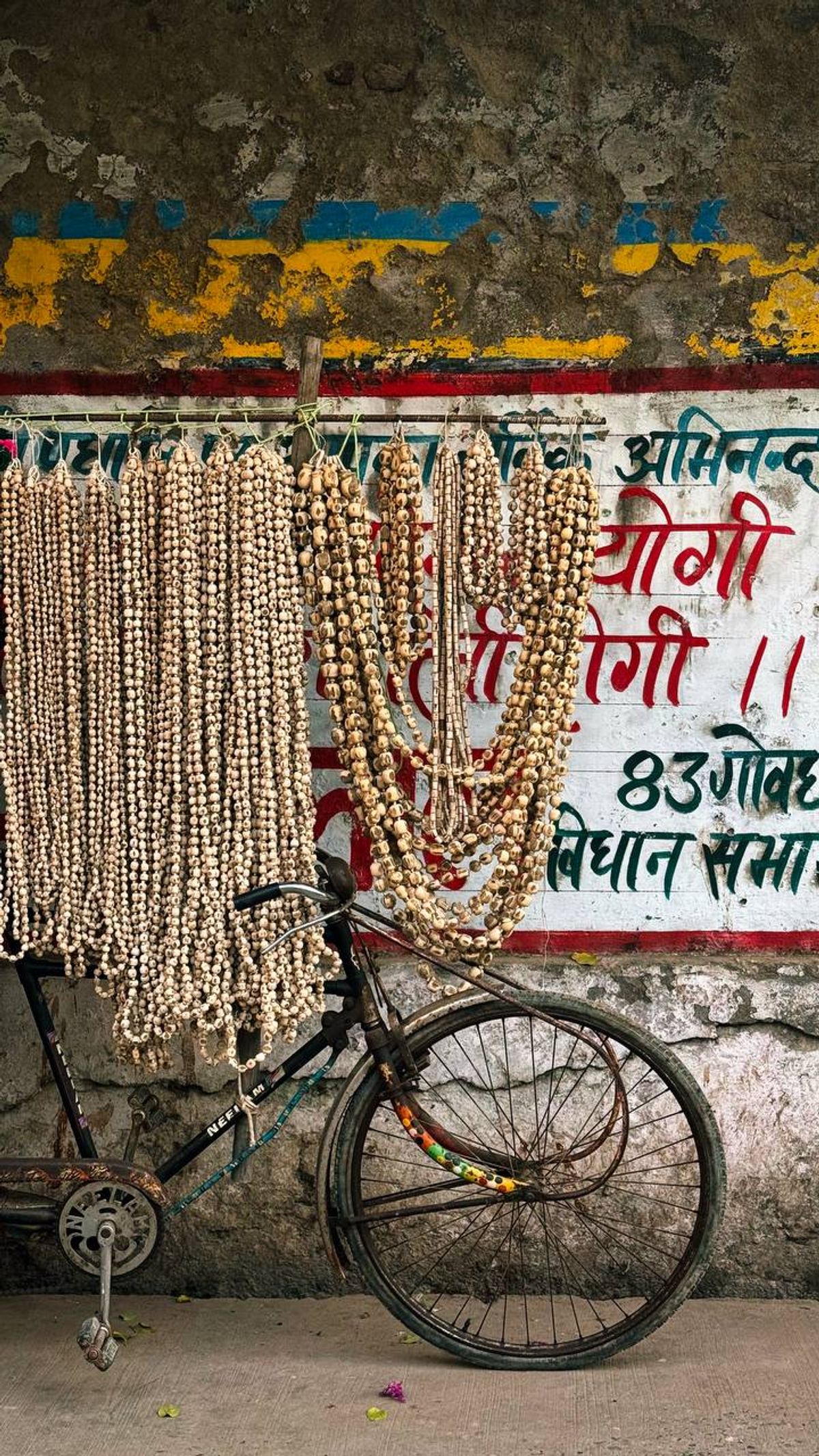 Prayer beads (mala) hanging on a bicycle against a colorful wall with Hindi text