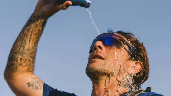 An endurance athlete pours water over their head to cool off in the summer heat