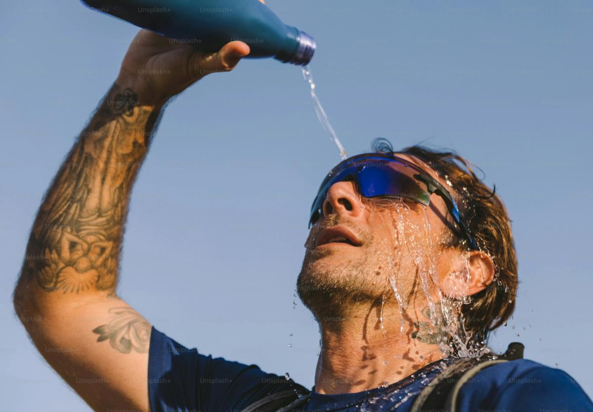 An endurance athlete pours water over their head to cool off in the summer heat