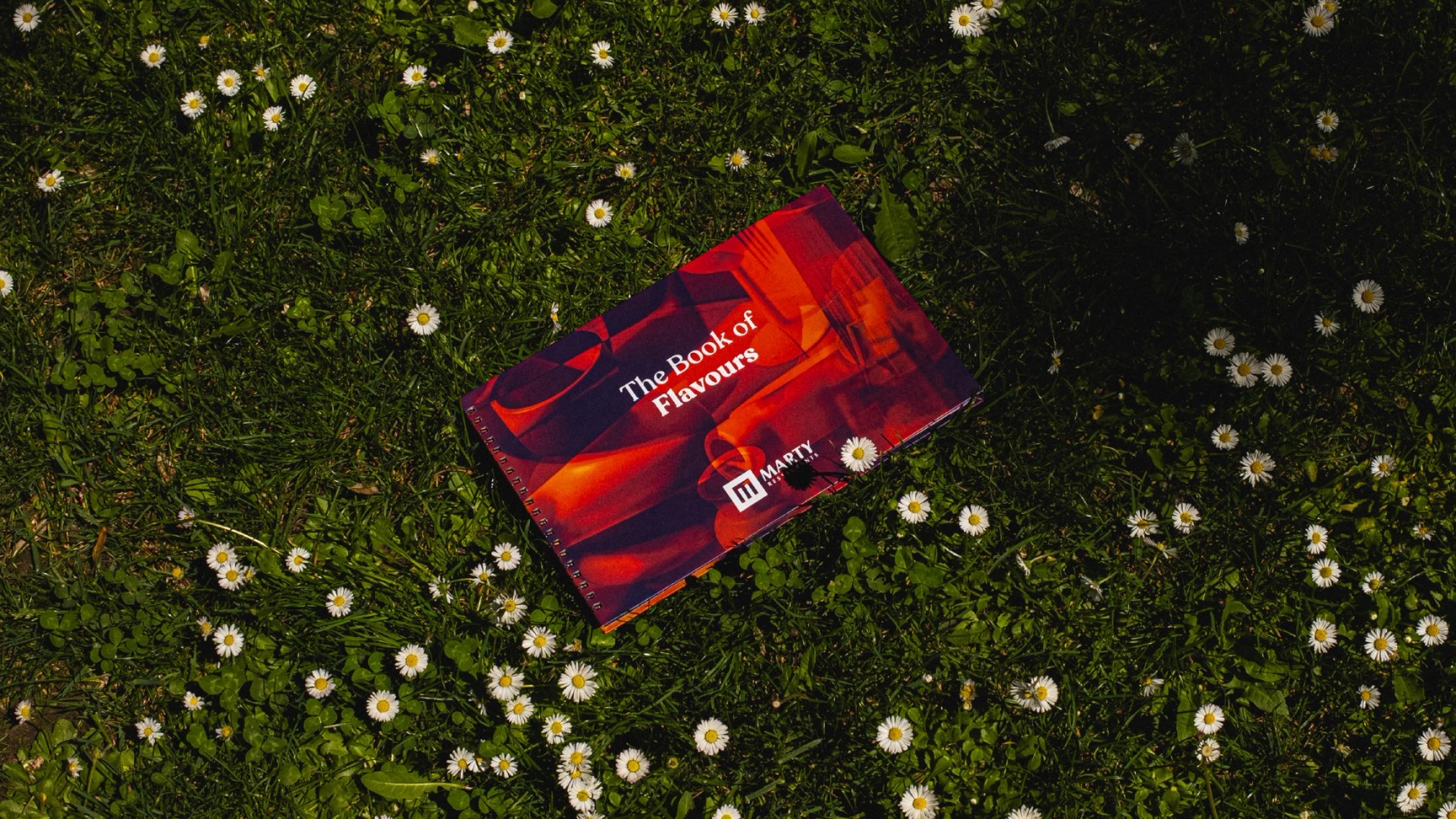 Marty Restaurants menu cover photographed on grass and small white flowers