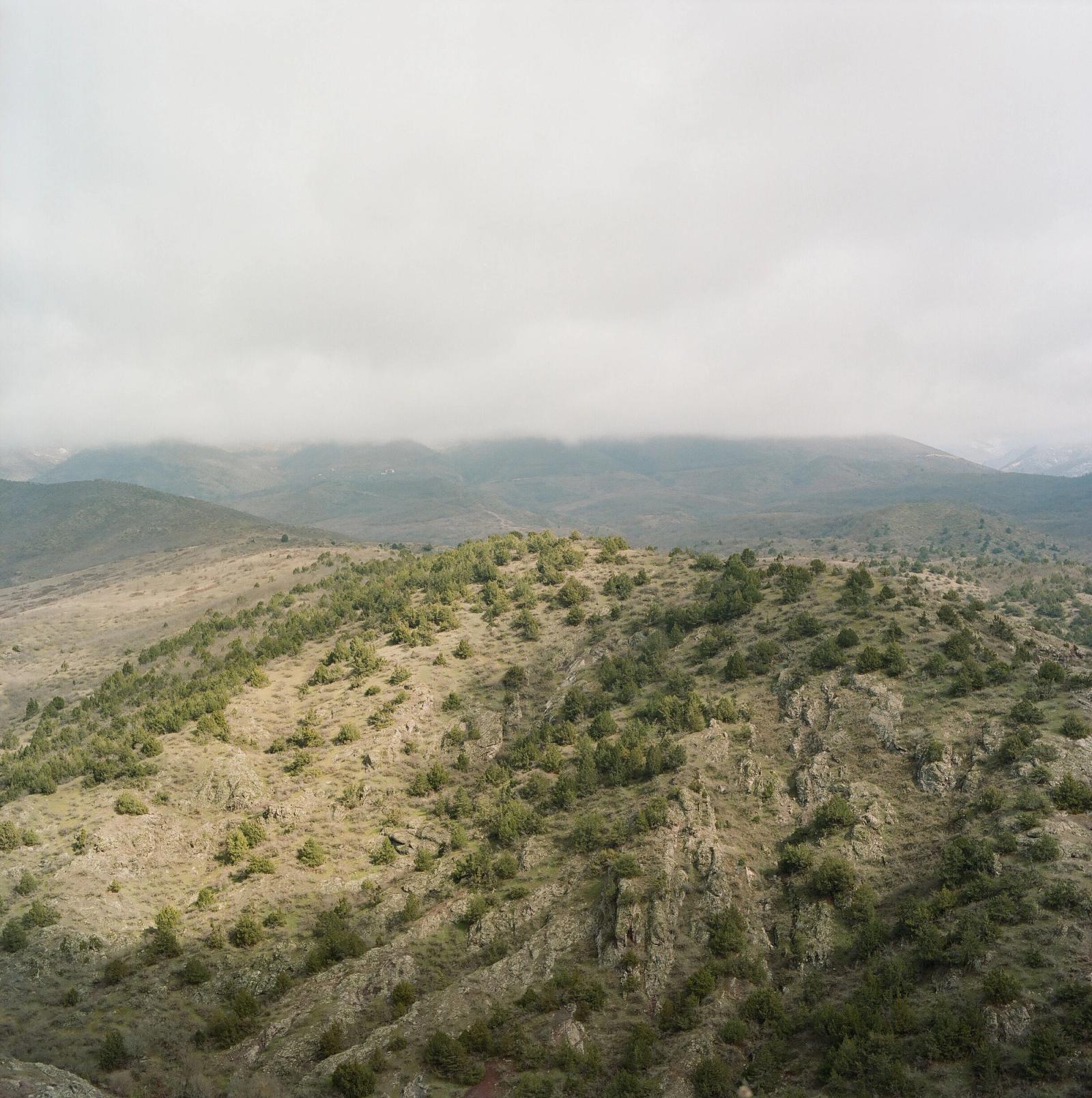Scrubby green hills under low cloud, with a range of mountains in the distance.