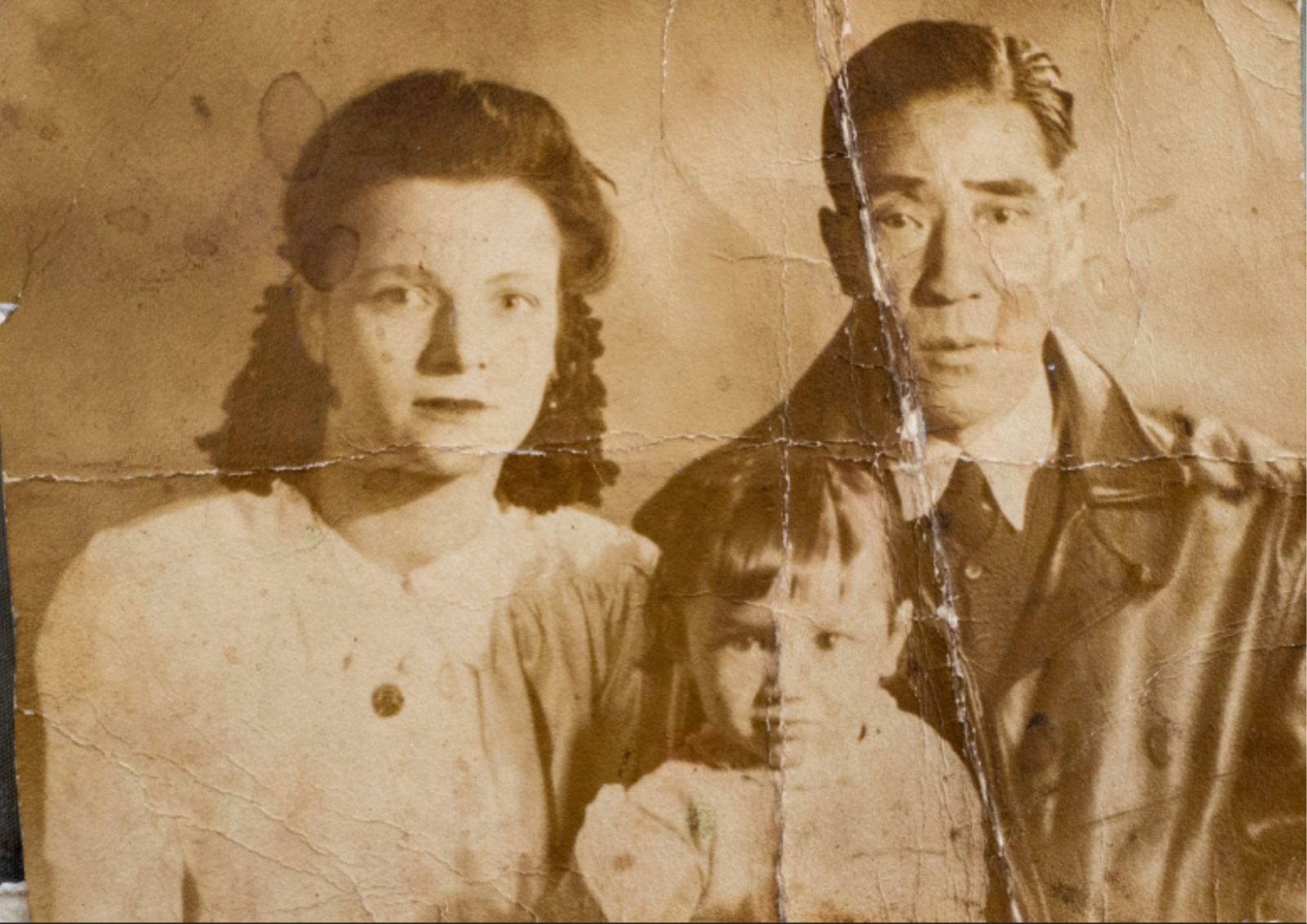 Cracked sepia family portrait of a woman and a man with a small child in front of them.