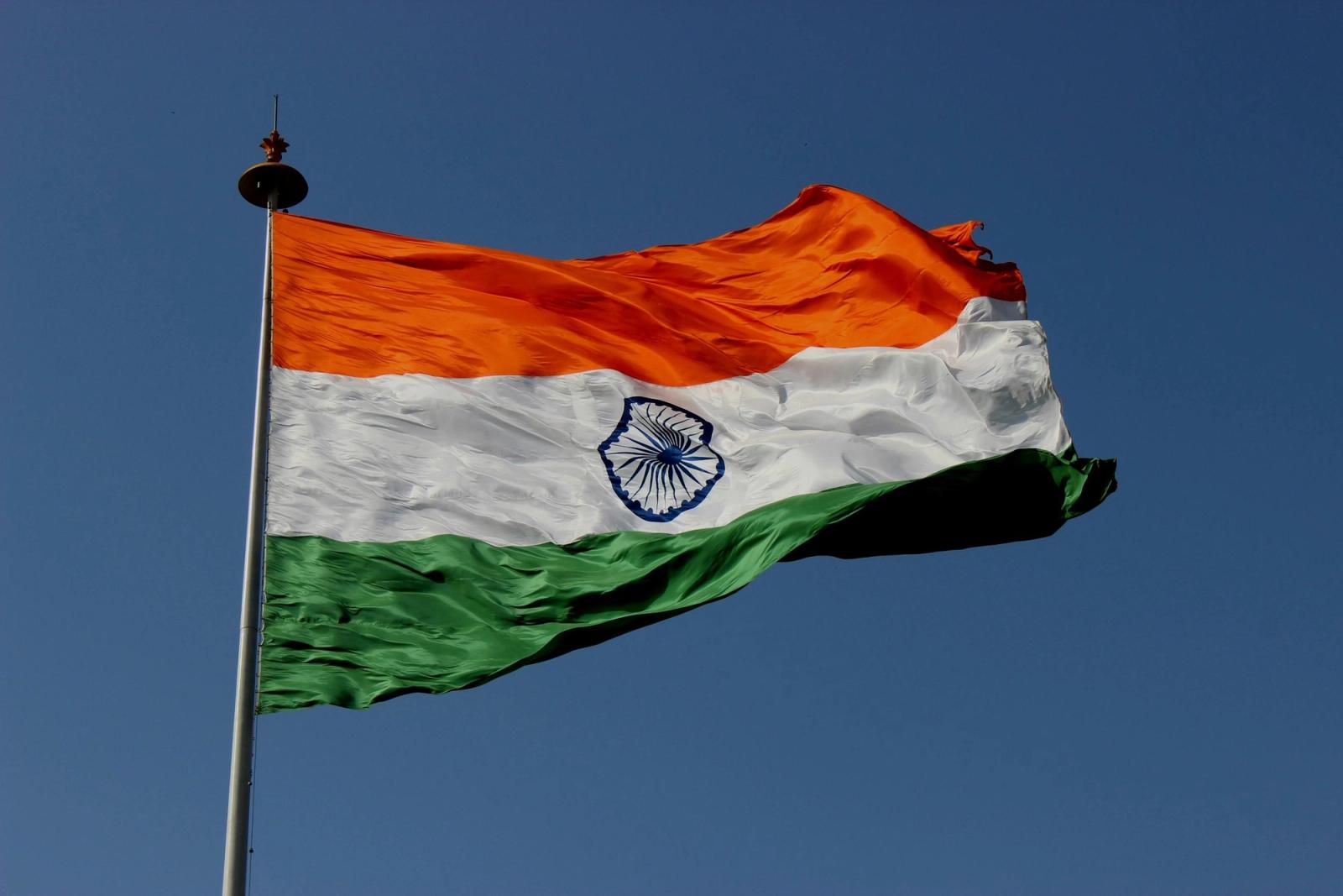 The Indian flag flying from a tall pole against a clear blue sky.