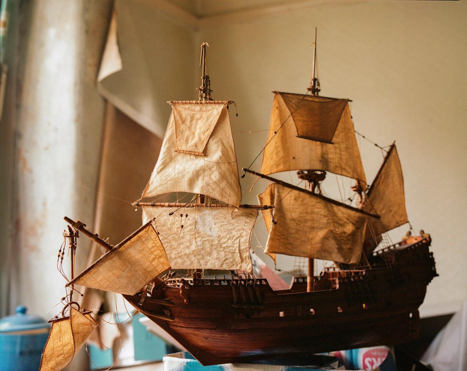 A detailed wooden model of a sailing ship with cream sails, on a shelf in a domestic room.