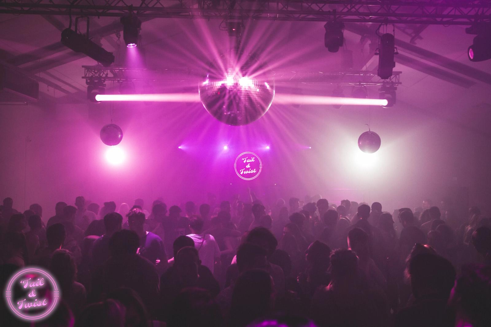A club crowd lit in purple, with a mirror ball and beams of light above the dance floor.