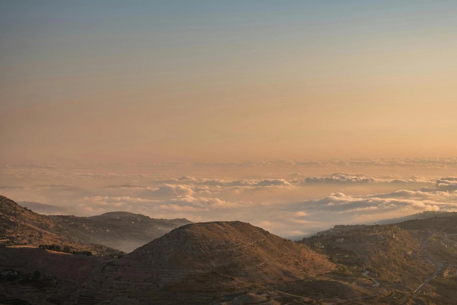 Golden evening light over rugged brown hills rising from a sea of cloud.