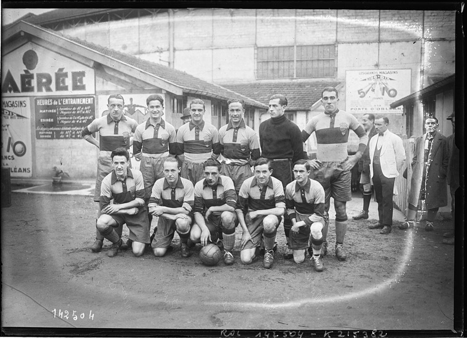 Black-and-white photograph of a football team in striped shirts posed in two rows, with a ball at their feet, in a yard.
