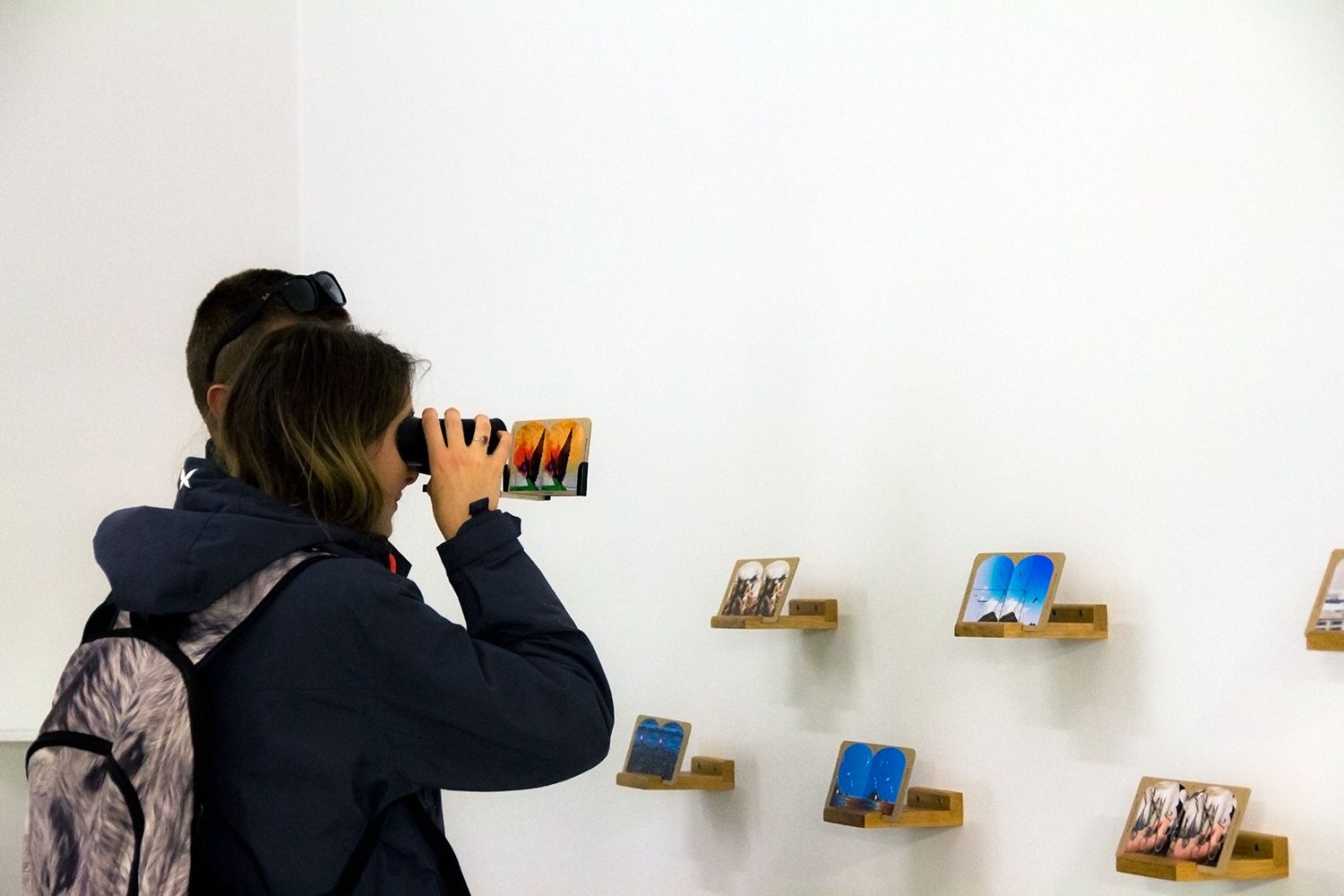 A visitor peers into a stereoscope. More stereoscope slides are affixed to the wall.