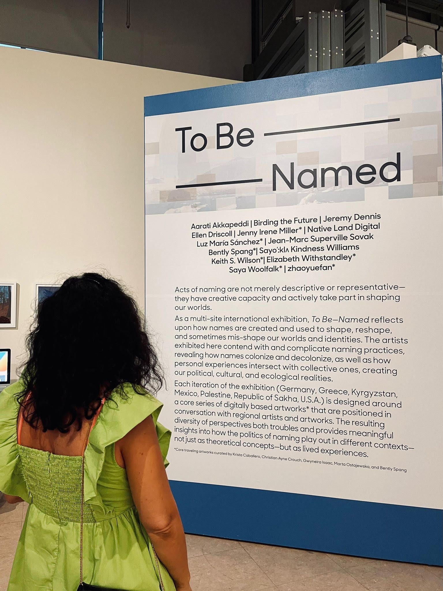 A person in a bright green dress looks at the exhibition introductory text
