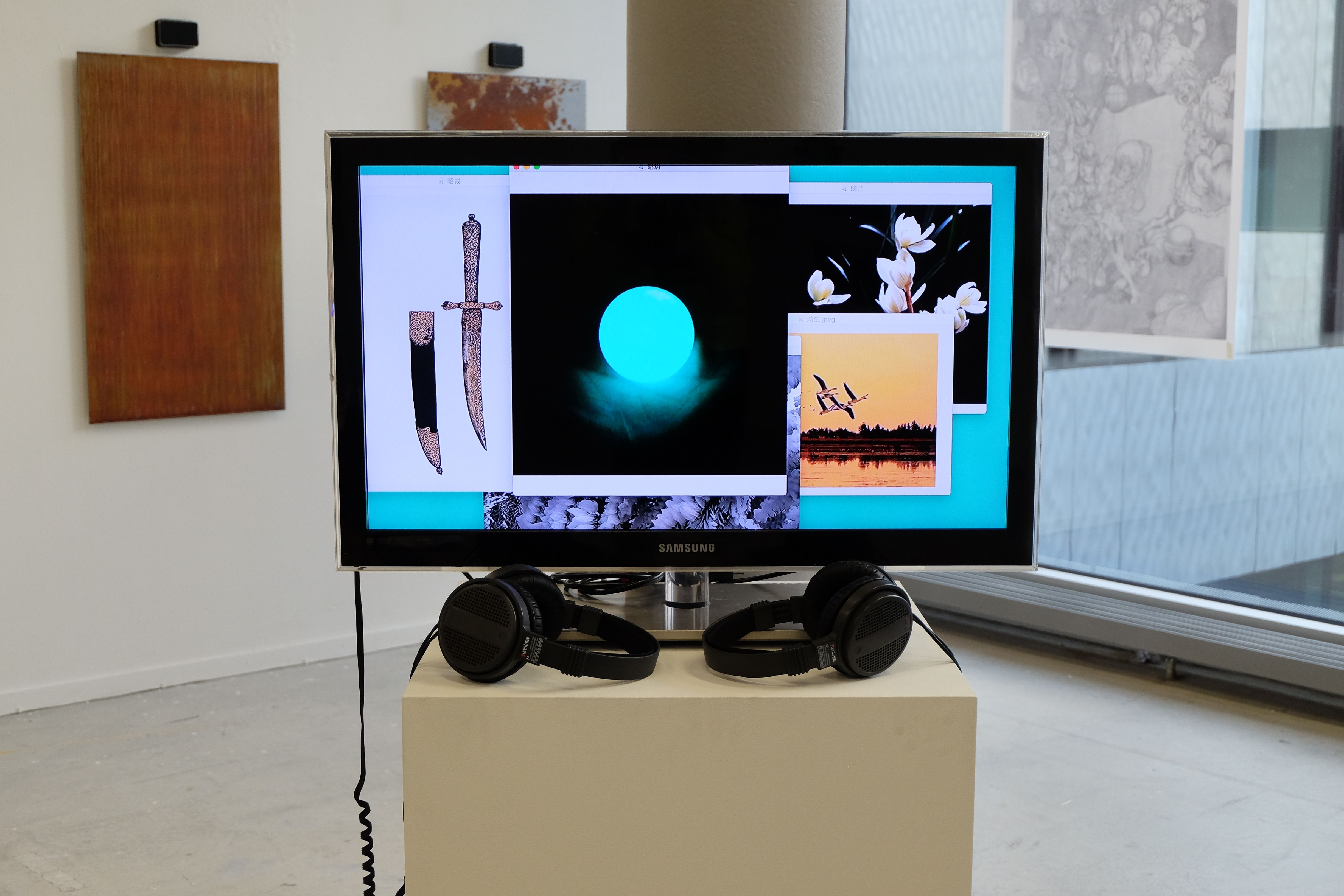 Monitor with two pairs of headphones in a gallery, showing a frame from Cage-Shining-Pearl