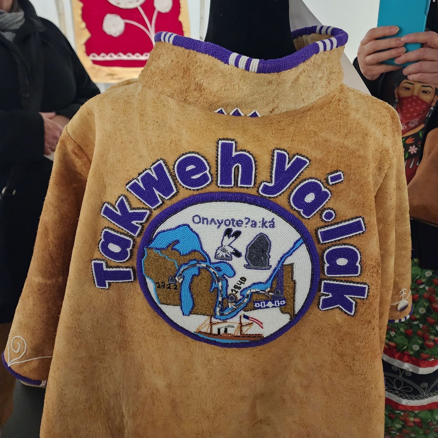 The back view of the jacket has beaded patch showing a journey through  the Great Lakes using quahog shell, also known as wampum beads, via steamboat