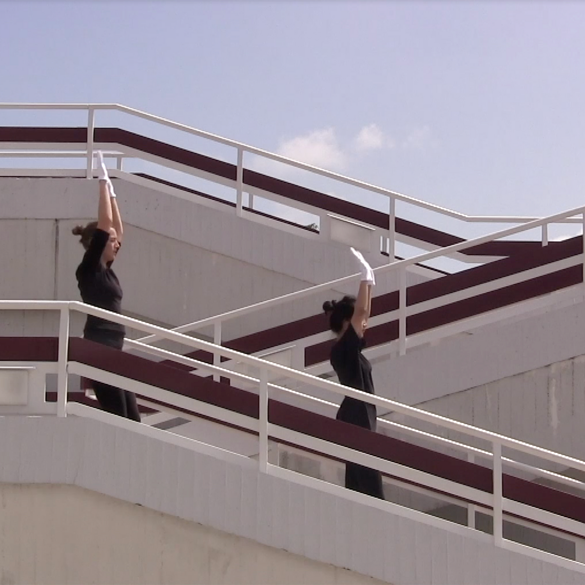 Two people dressed in black with white gloves, walking down a flight of stairs with their hands raised