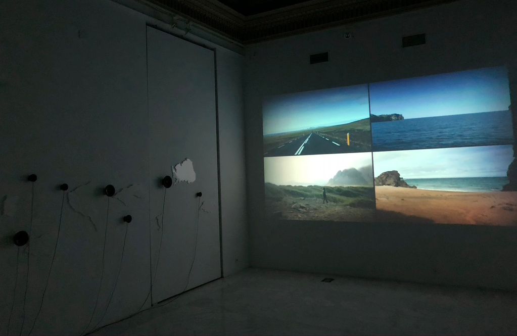 A dark room with a video installation projected: four landscapes on the wall