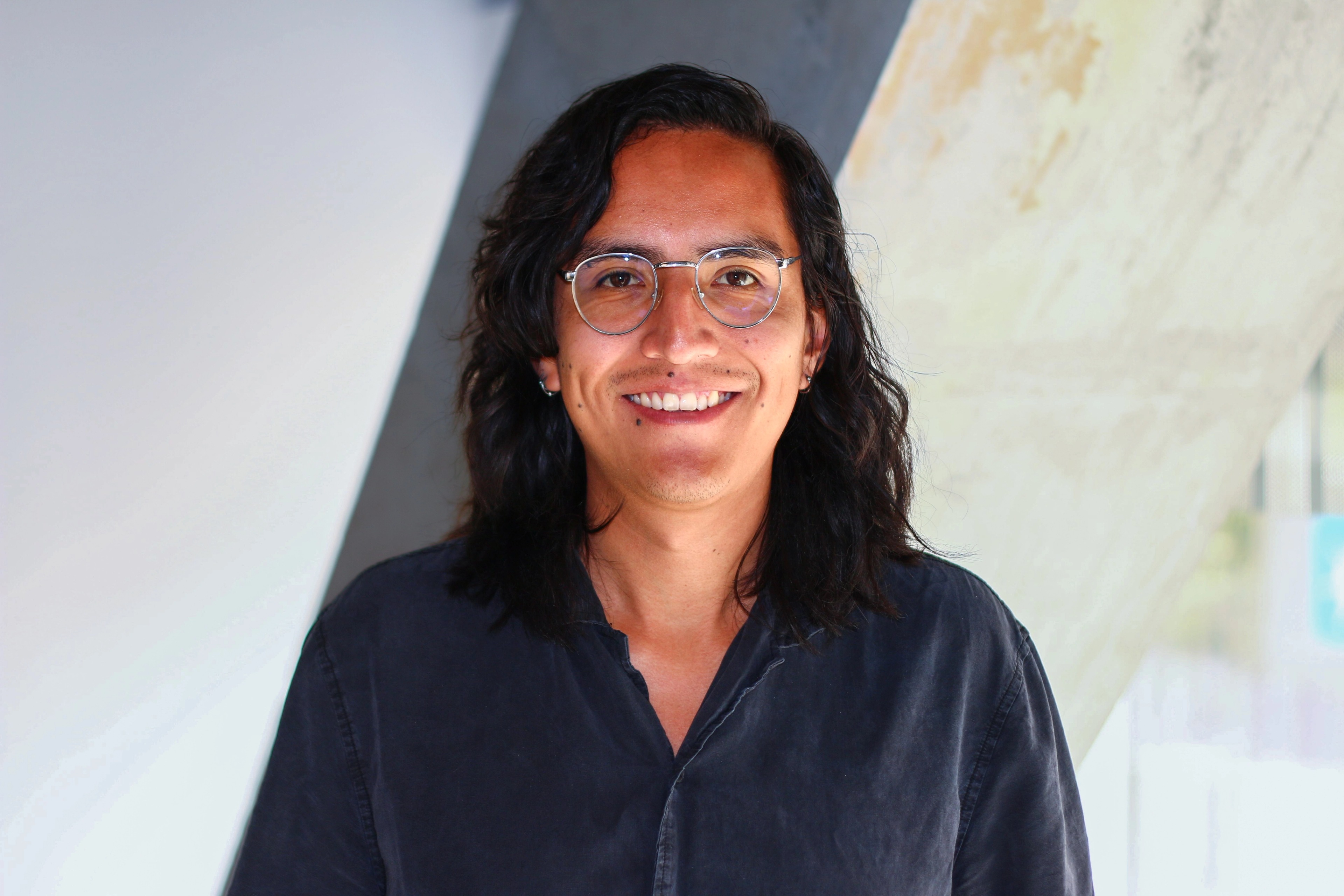Portrait of Mateo Ochoa Coloma, Software Developer at Ava Industries, smiling and wearing glasses with dark hair, standing in a modern office environment.
