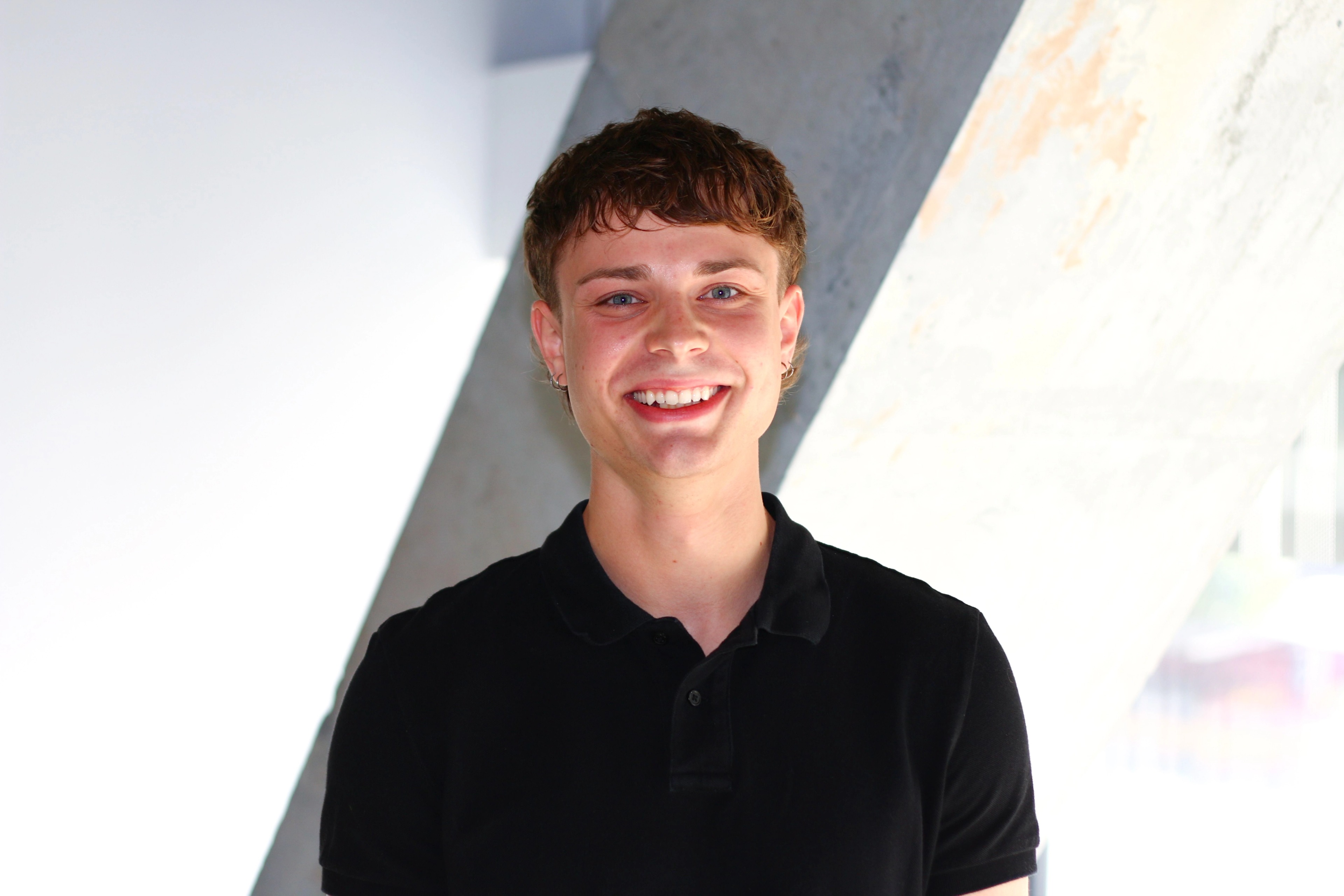 Portrait of Griffin Graham-Bennett, Customer Support Analyst Intern at Ava Industries, smiling in a modern office environment wearing a black polo shirt.