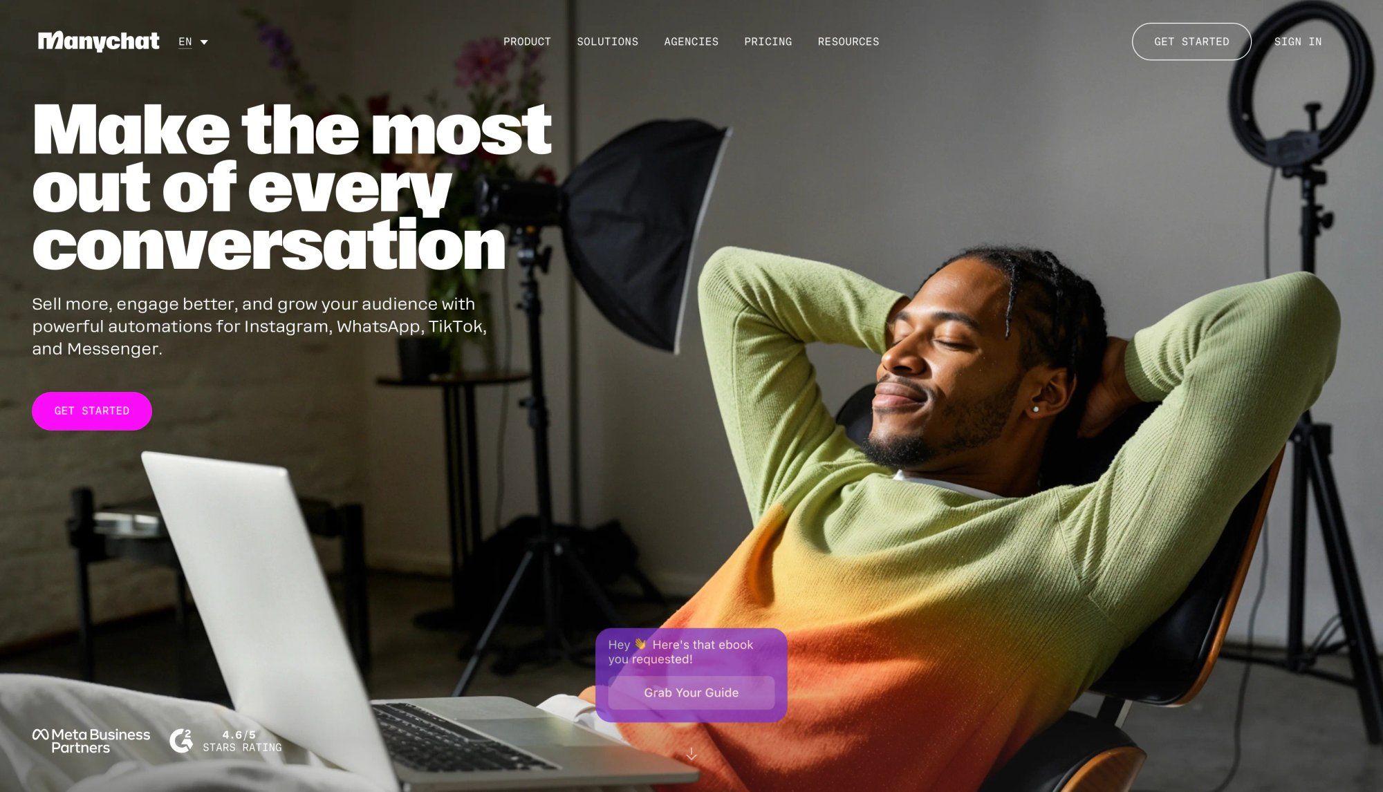 A man in a gradient sweater relaxes in a chair with a laptop, studio lighting, and website content.