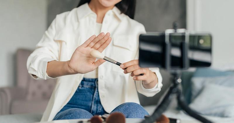 A female content creator filming a makeup tutorial with a phone, showcasing a brush as part of influencer-marketing-campaigns.