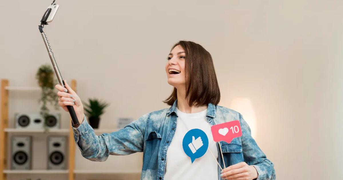 A female content creator smiling while taking a selfie with a phone on a stick, symbolizing the differences between KOC and KOL in influencer marketing.