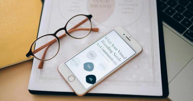 A smartphone displaying branding tips, placed on a desk with glasses, notebook, and laptop, representing influencer marketing strategies.