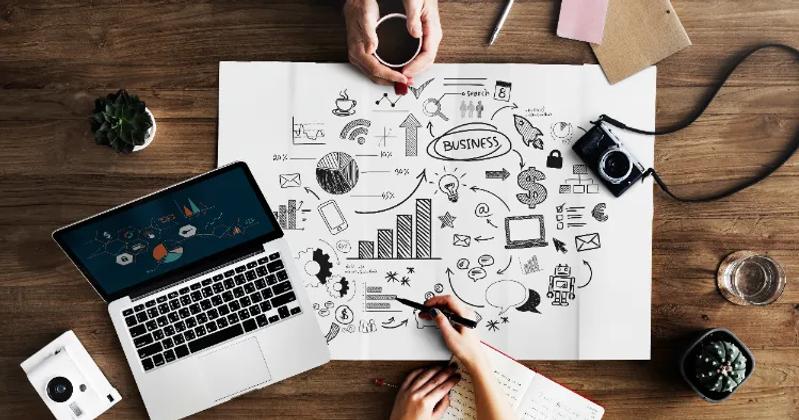 A top-view of a workspace with a laptop, camera, and a business strategy sketch, representing influencer marketing tools for campaign management and analytics.