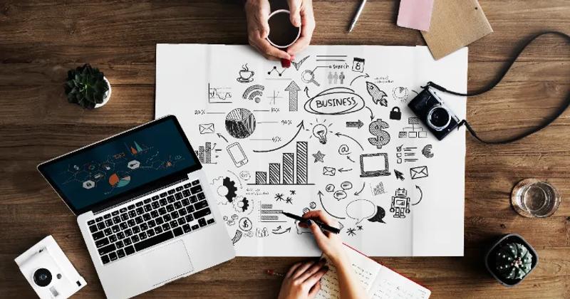 A top-view of a workspace with a laptop, camera, and a business strategy sketch, representing influencer marketing tools for campaign management and analytics.