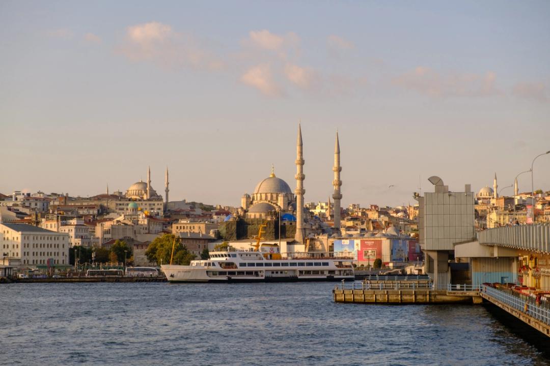 A Bosphorus ferry docked at Eminönü with Istanbul's mosque-topped skyline behind it at golden hour
