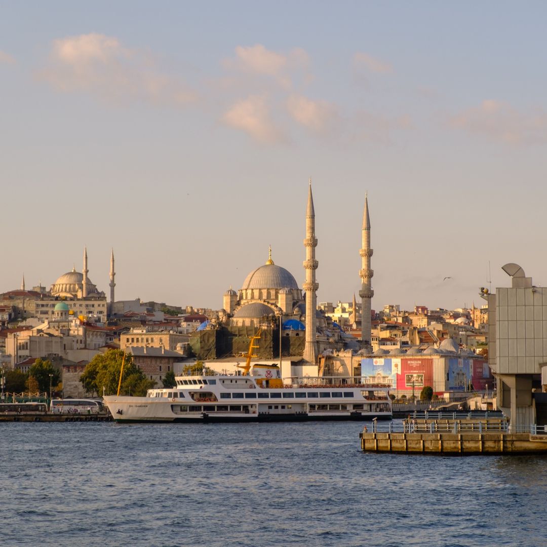 A Bosphorus ferry docked at Eminönü with Istanbul's mosque-topped skyline behind it at golden hour