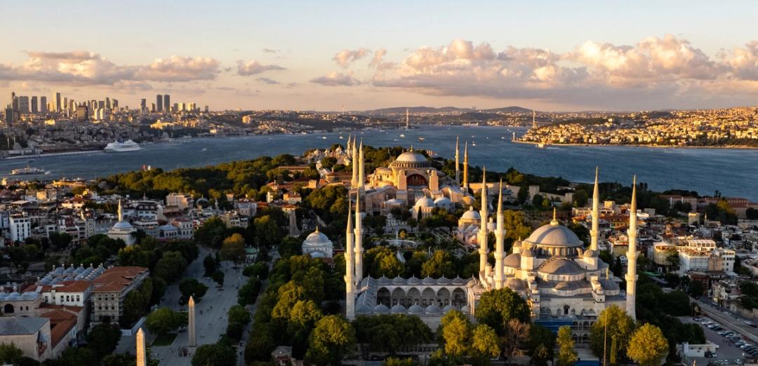 Aerial view of Hagia Sophia and the Blue Mosque on Istanbul's historic peninsula, with the Bosphorus and the modern skyline beyond at golden hour