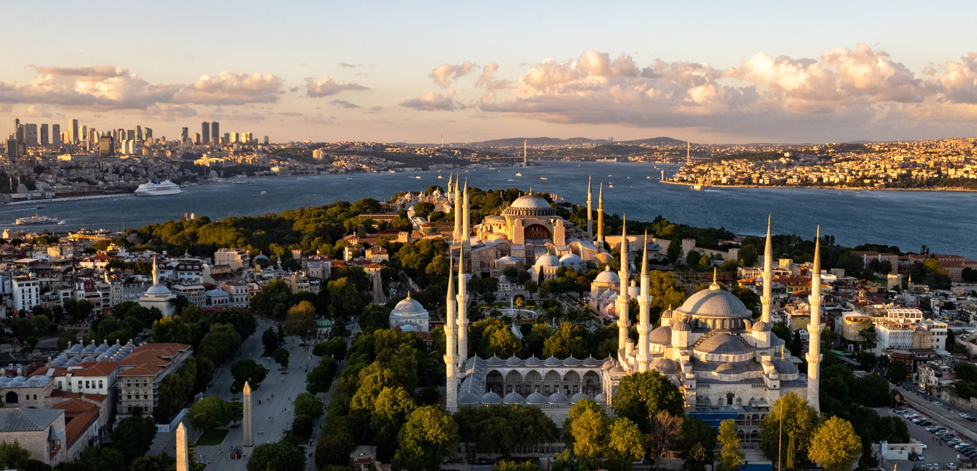 Aerial view of Hagia Sophia and the Blue Mosque on Istanbul's historic peninsula, with the Bosphorus and the modern skyline beyond at golden hour