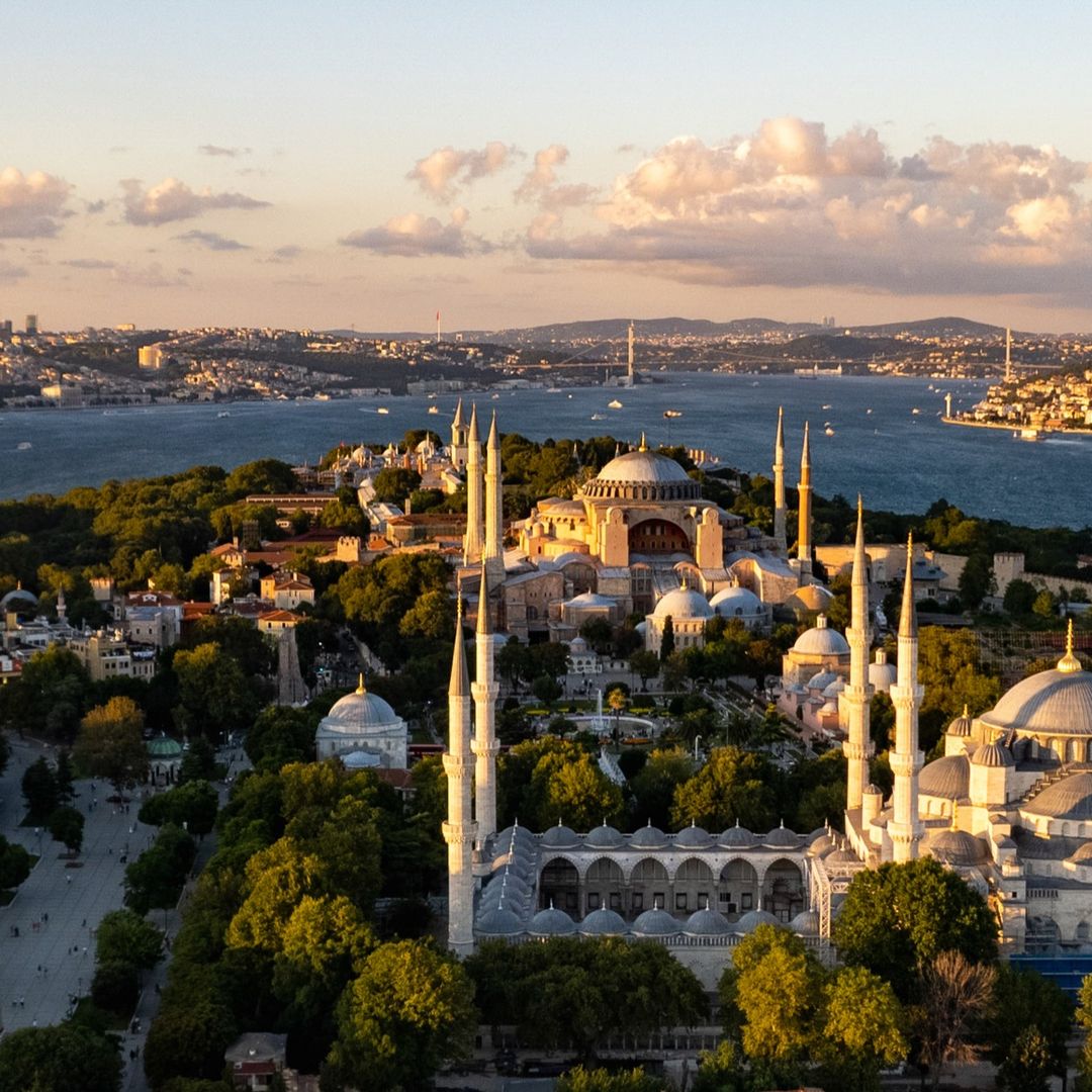 Aerial view of Hagia Sophia and the Blue Mosque on Istanbul's historic peninsula, with the Bosphorus and the modern skyline beyond at golden hour