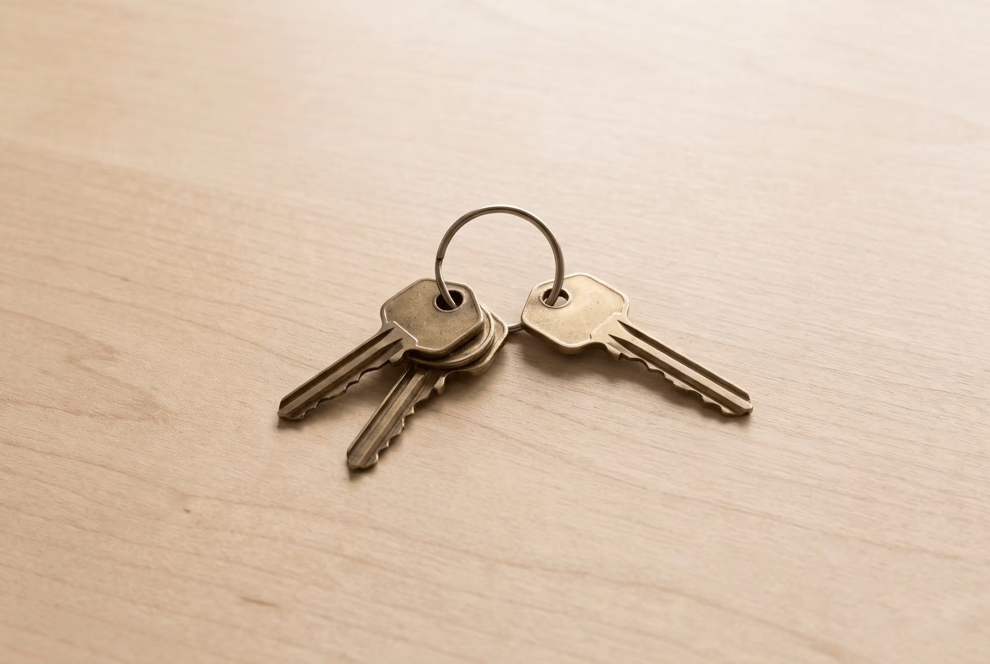 Four brass keys on a wooden table, one set slightly apart from the other three.