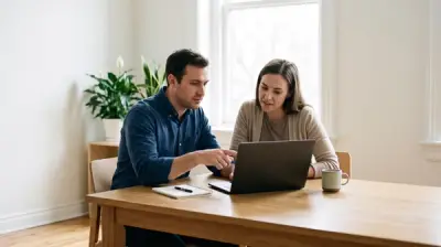 A man and a woman at a wooden table reviewing something on a laptop together, with a notebook and coffee mug beside them