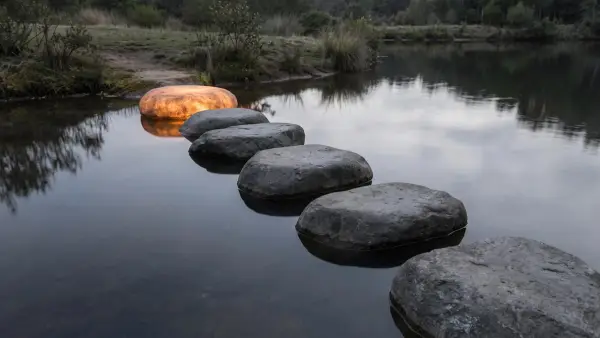 A row of stepping stones across still water, with only the last stone glowing.