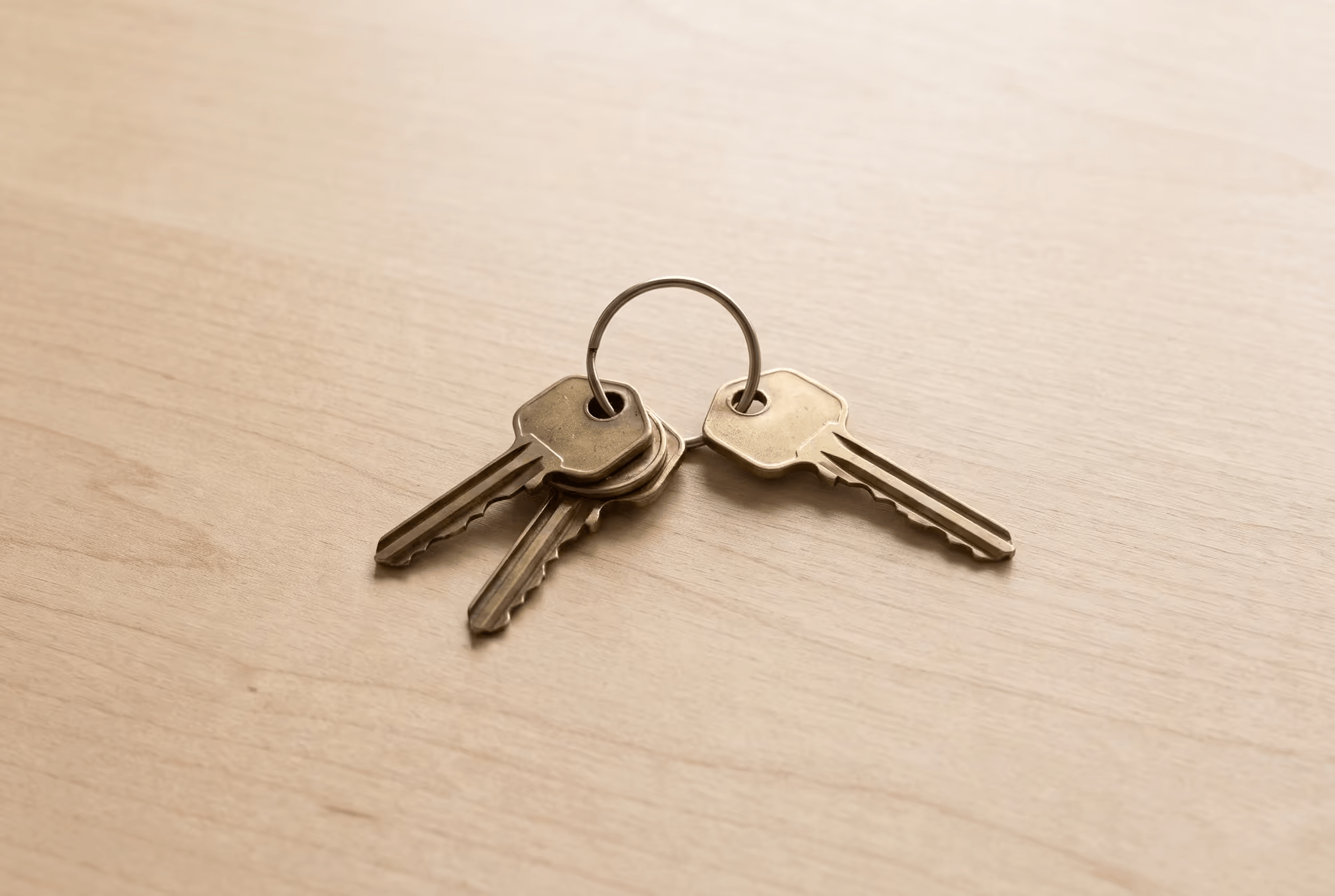 Four brass keys on a wooden table, one set slightly apart from the other three.