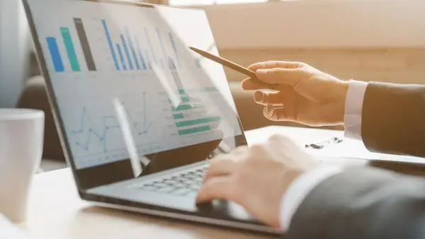 Person pointing at a chart on a laptop screen during a presentation or discussion