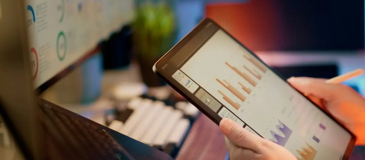 Person reviewing financial charts and graphs on a tablet in a modern office workspace