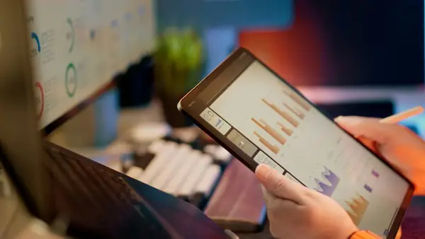 Person reviewing financial charts and graphs on a tablet in a modern office workspace