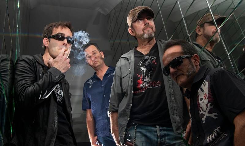 Cinco músicos del rock lanzaroteño posan con gafas de sol y chaquetas ante paneles de espejo; uno fuma.