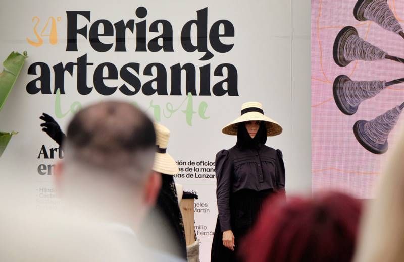 Modelo con sombrero de paja y ropa negra desfila ante el panel de la 34ª Feria de Artesanía de Lanzarote.
